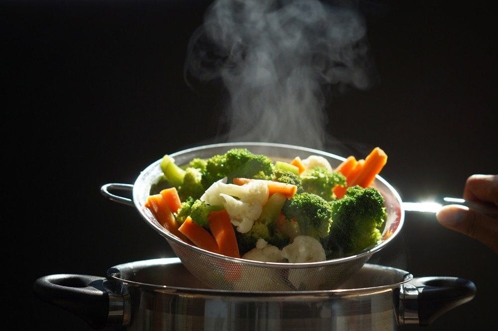 Freshly cooked broccoli, cauliflower, and carrot pieces in a basket after steaming