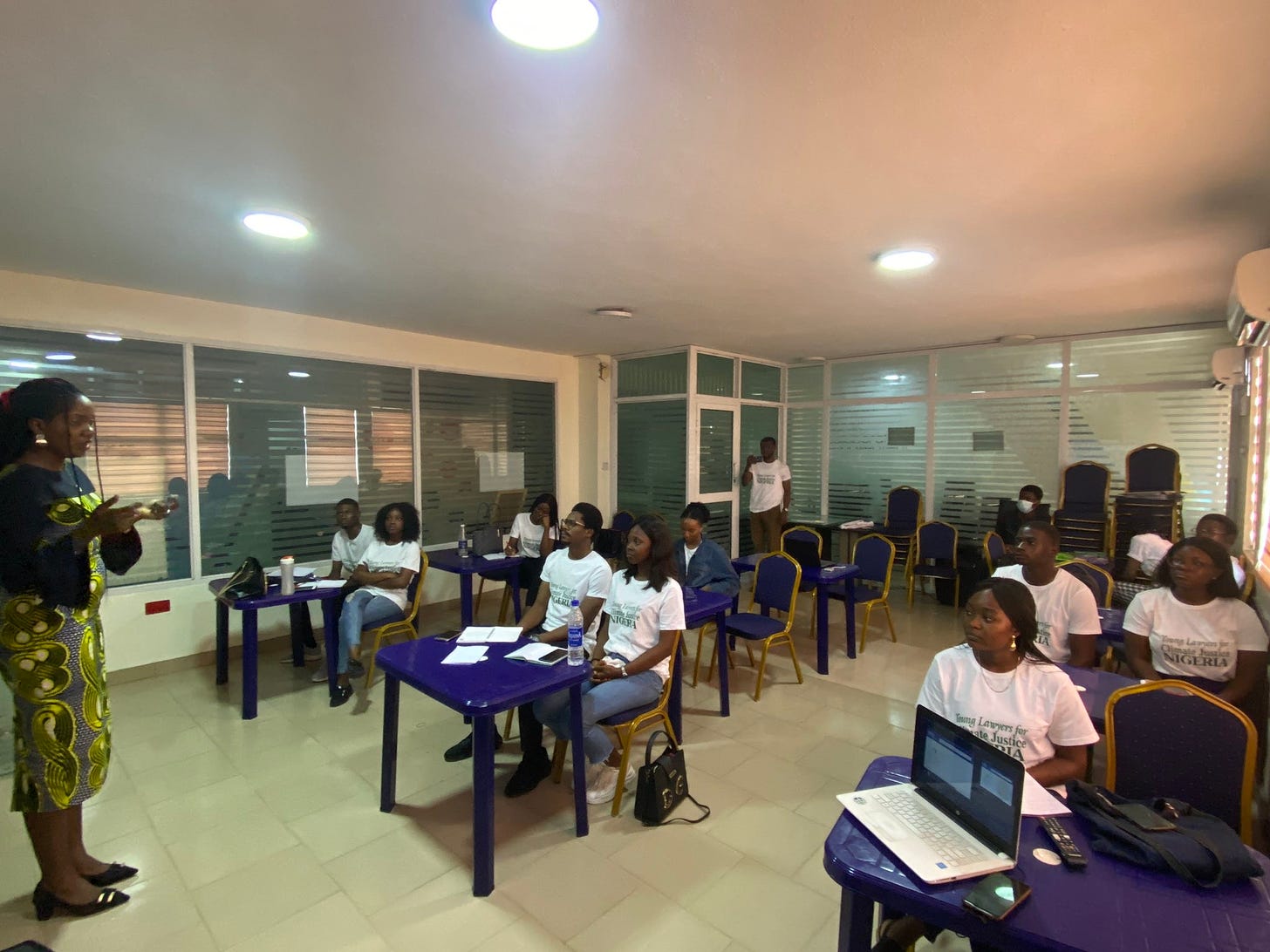 A classroom in Nigeria with a woman teaching a group of students in a uniform of white shirts and jeans