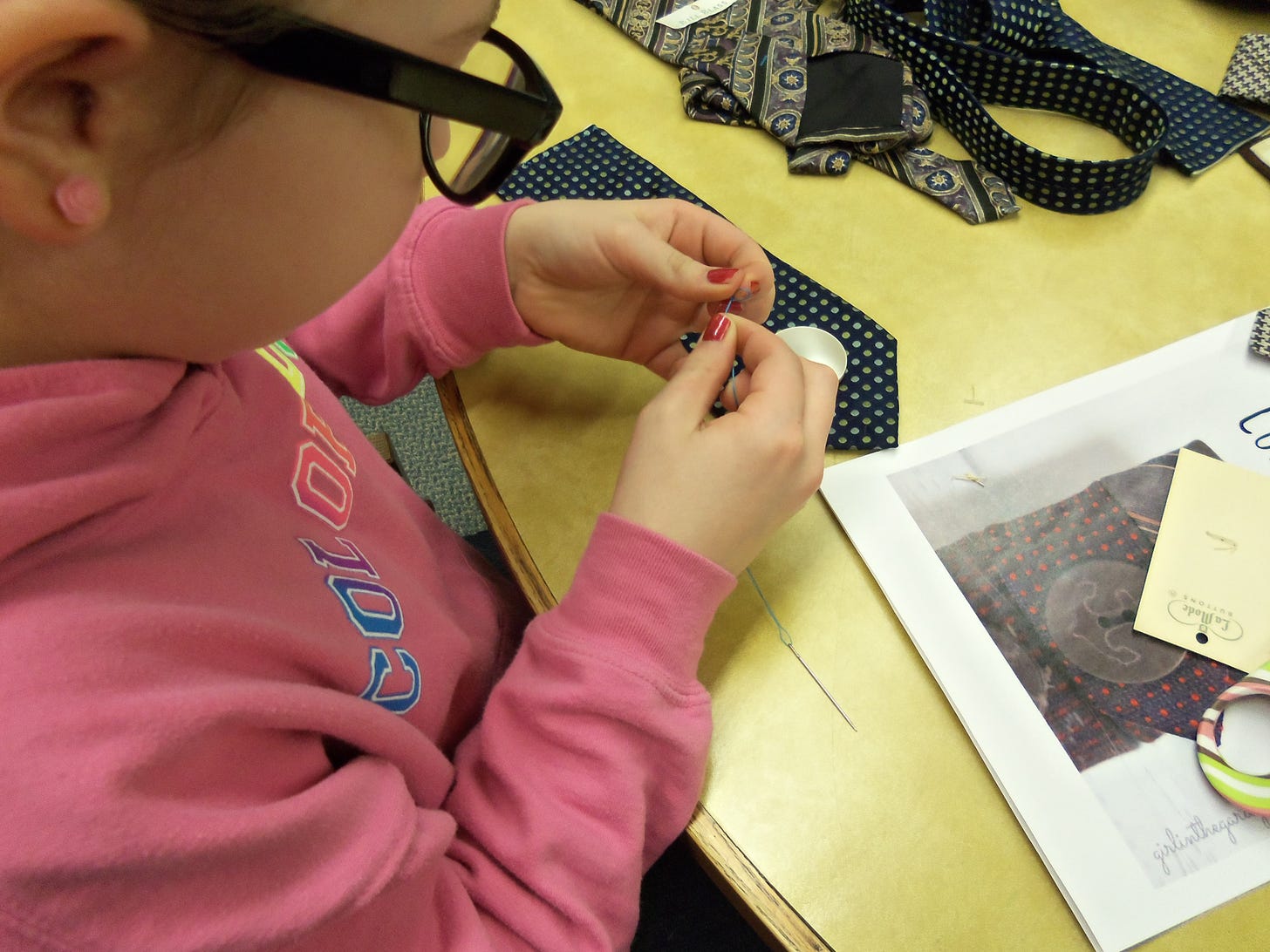 A young visitor works on a sewing project at a table in a library makerspace.