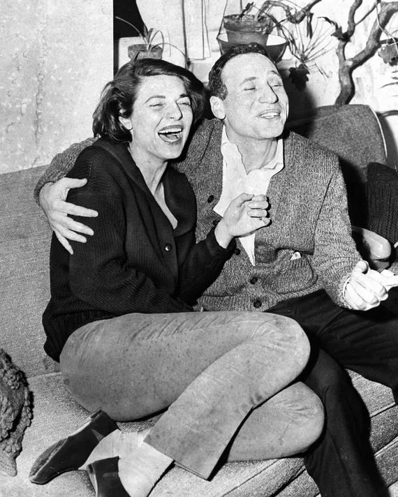 Image: A black and white photo of a young Anne Bancroft and Mel Brooks with his arm around her, both laughing