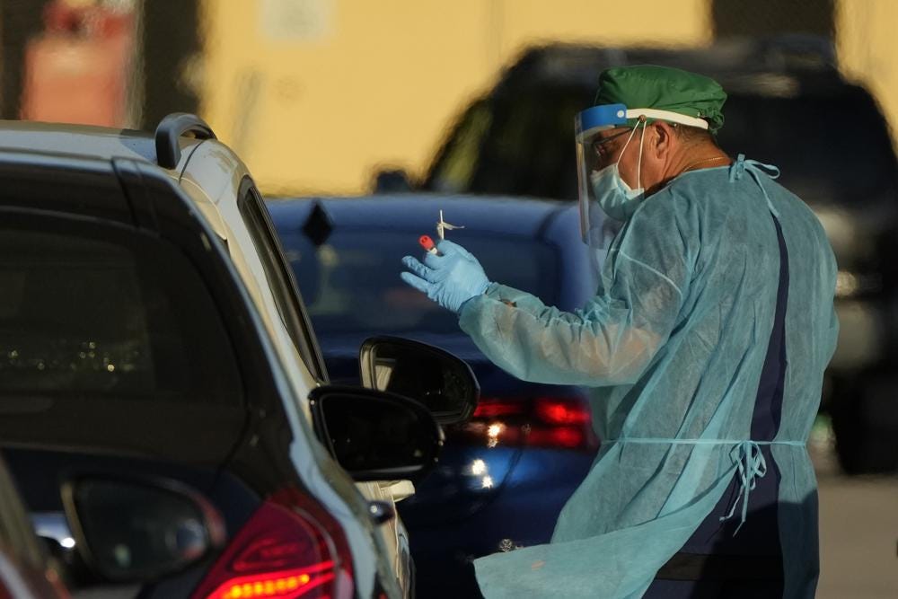 A health care worker tests people for COVID-19 at a drive-up testing center at Tropical Park, Wednesday, Dec. 29, 2021, in Miami. (AP Photo/Rebecca Blackwell)
