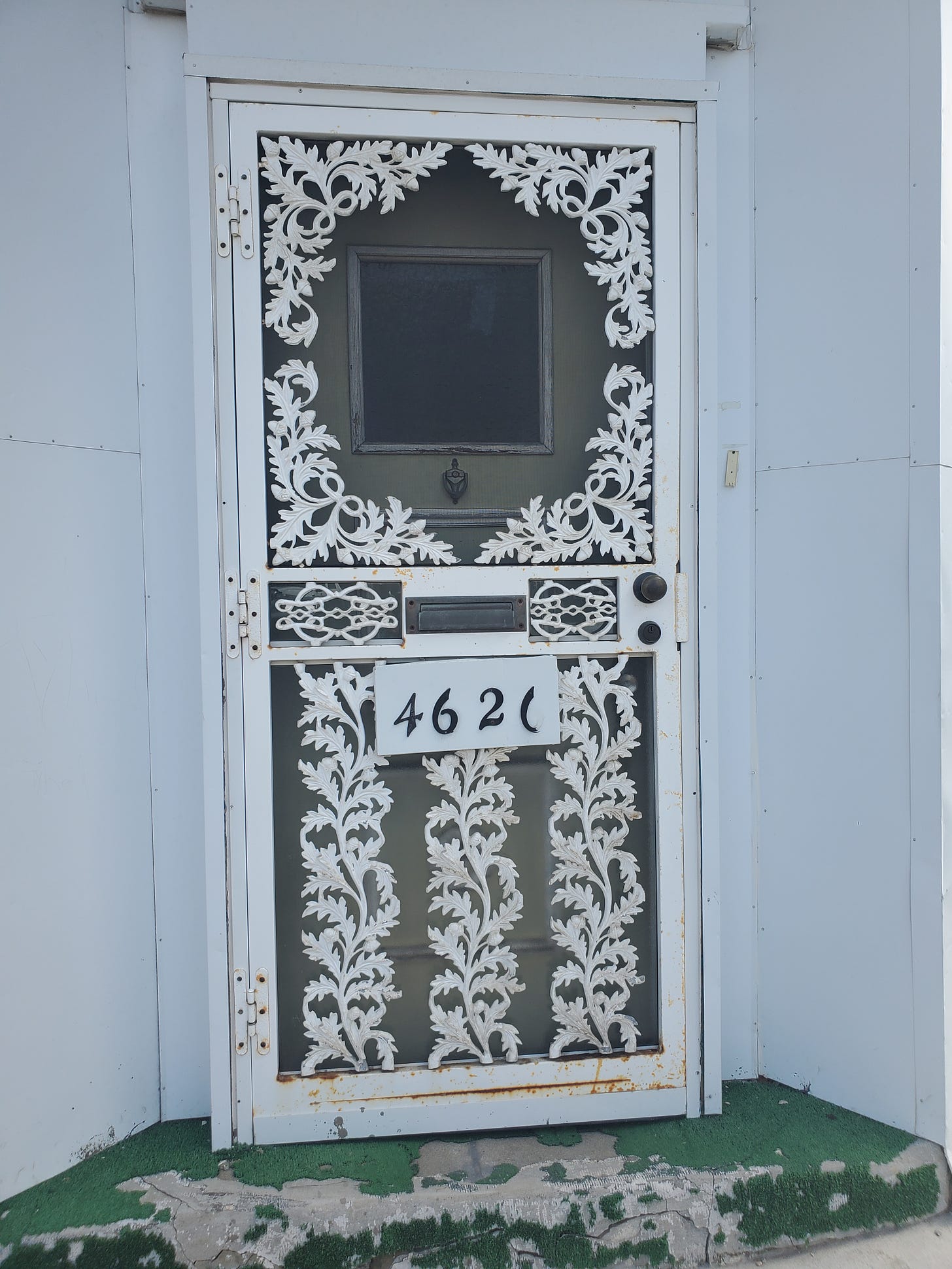 A white door with ornate ironwork reminiscent of feathers or leaves. The number 4621 is on the front of the door.