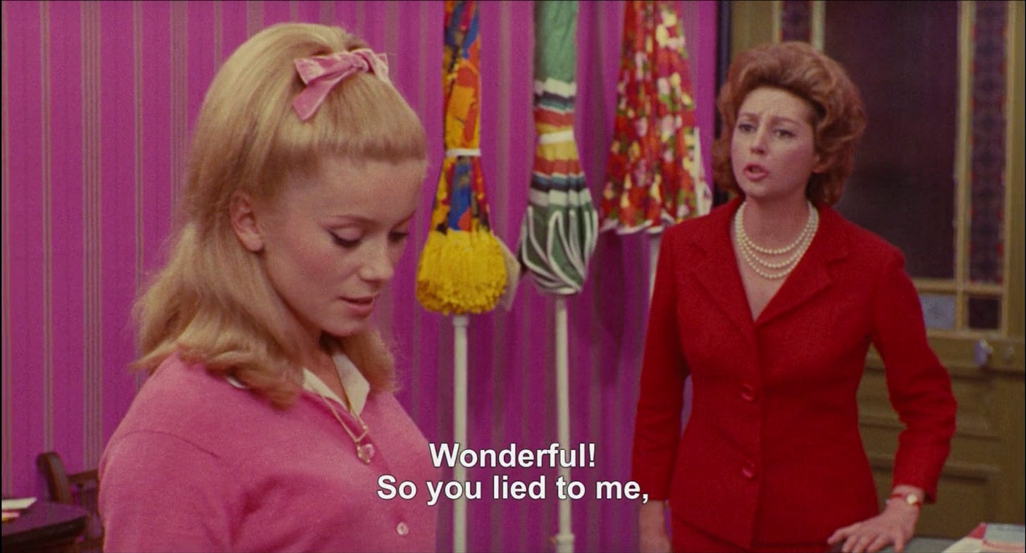 Geneviéve and her mother inside the umbrella shop with its bright pink wallpaper