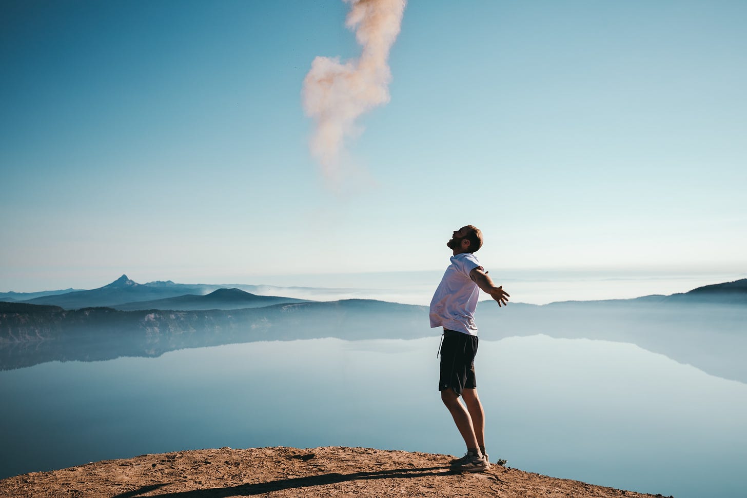 A white man stands in front of a mountain lake and jumps with his arms kind of behind him. He looks really happy but in a very corporate, posed kind of way