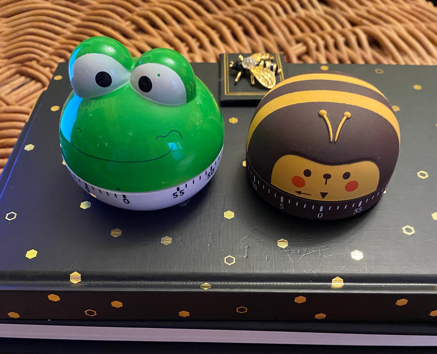 A frog-shaped timer and a bee-shaped timer, sitting on a notebook