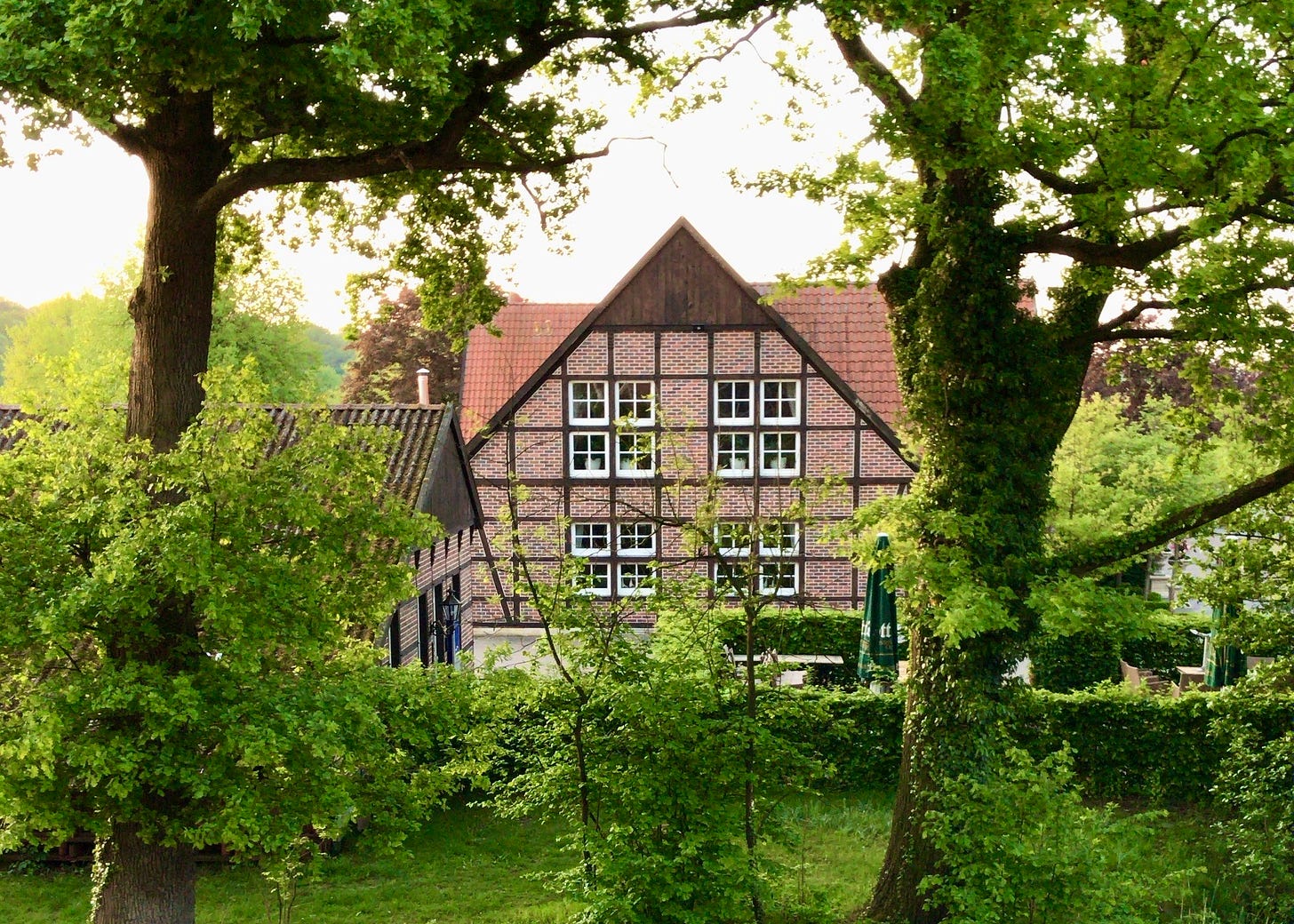 A red-brick building with half-timbered wood elements visible through lots of bright green trees