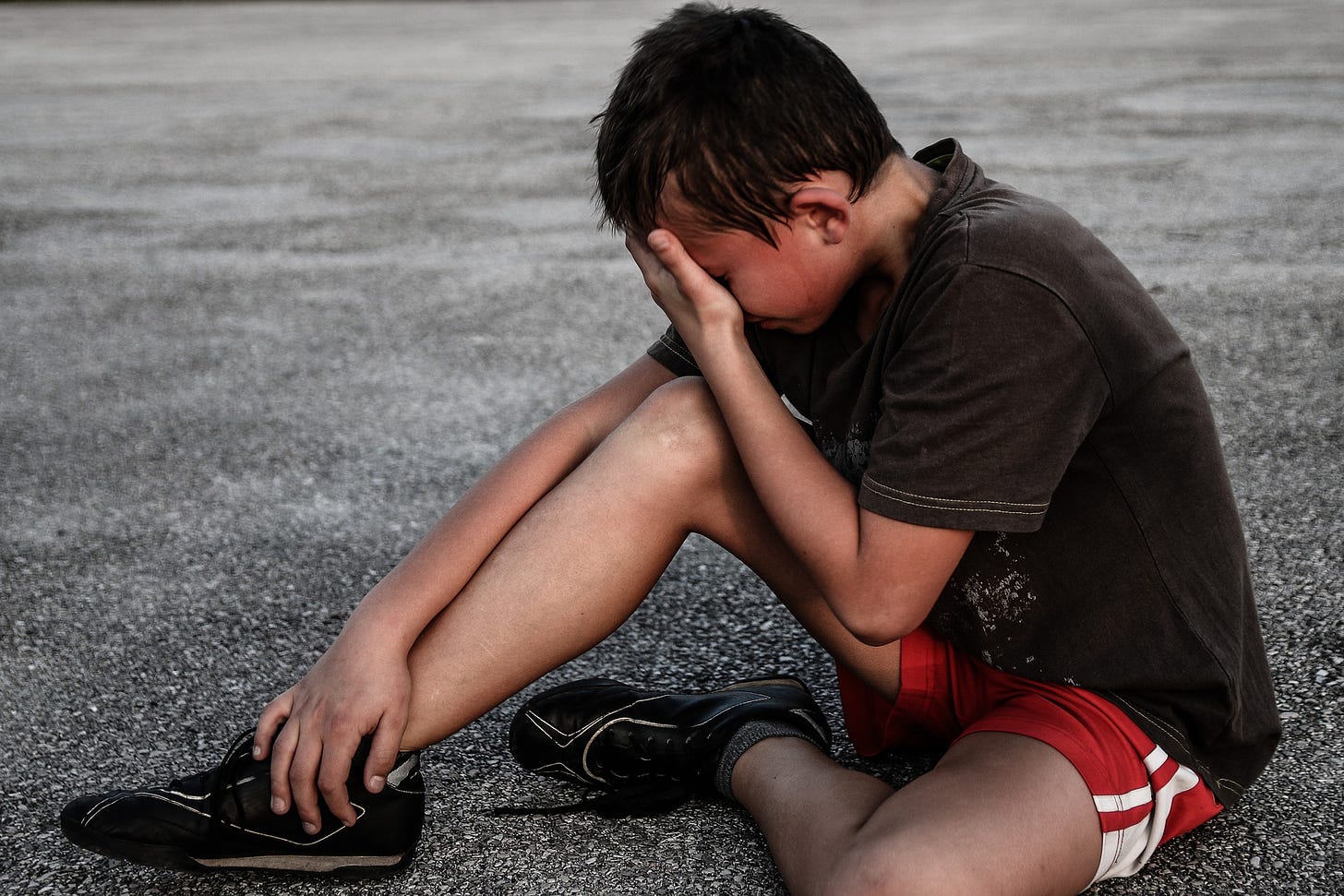 Boy sitting on asphalt head in hands red shorts black tee shirt