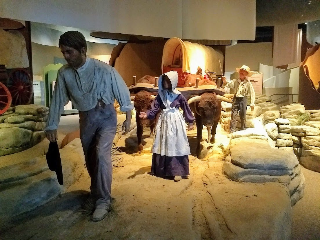 Museum tableau of family group walking through desert with wagon  and oxen