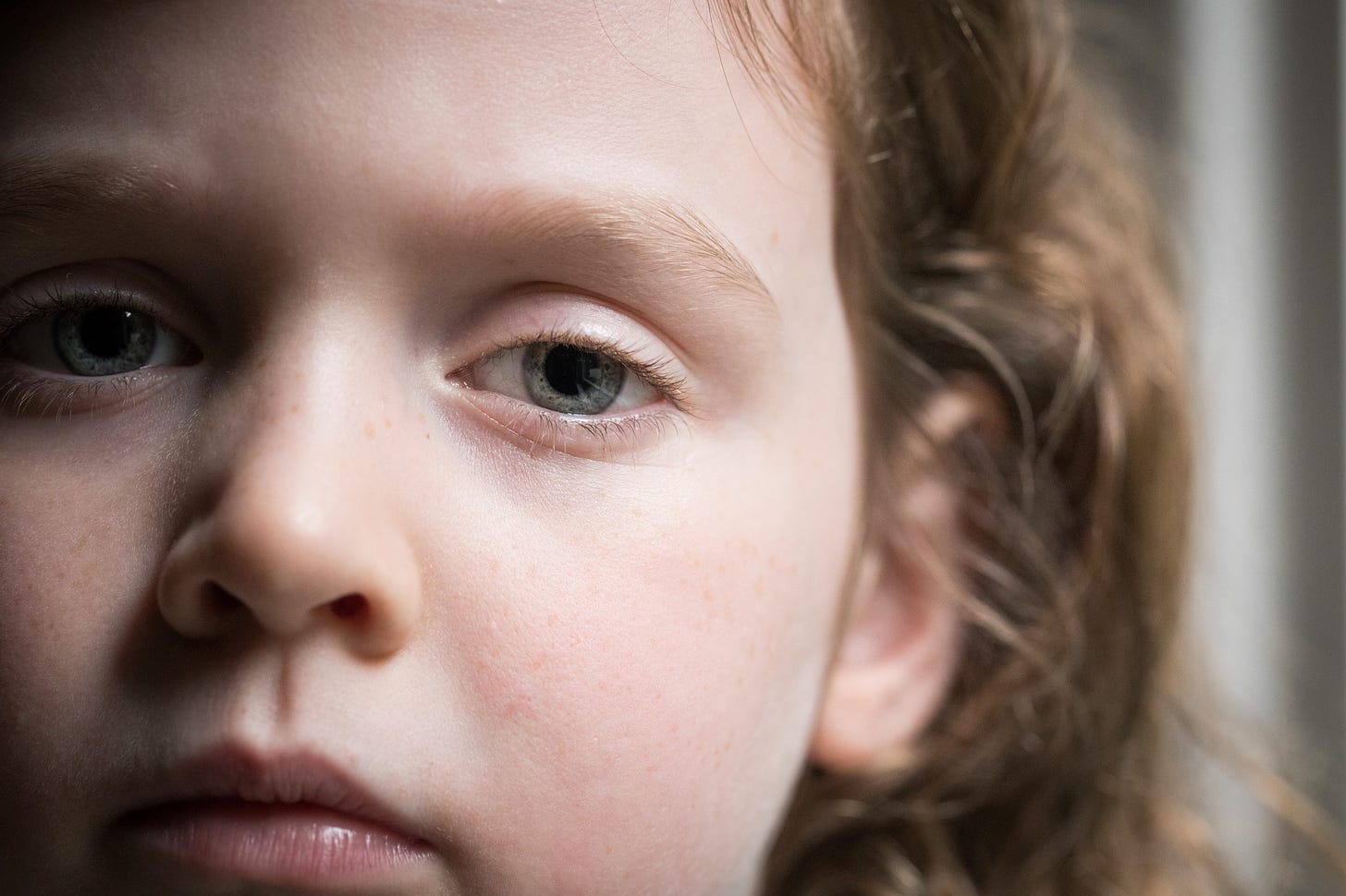 A young child with curly red hair stares sadly at the camera in a close up.