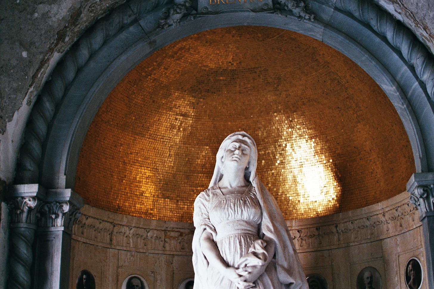 A statue of the Madonna sits inside a niche in the wall, with golden reflective tiles behind her head and shoulders.