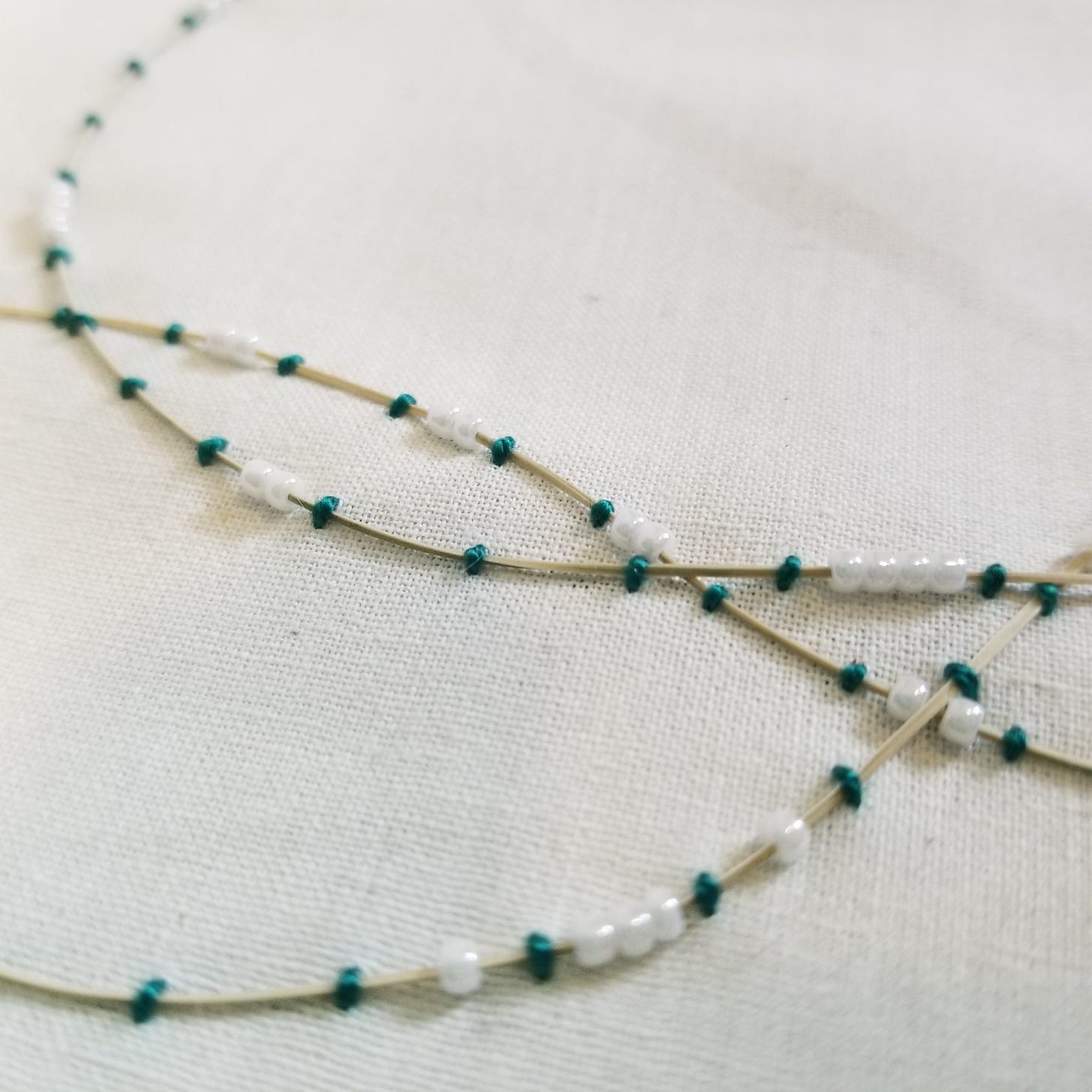 dried grass couched onto muslin fabric  with green thread and white glass beads