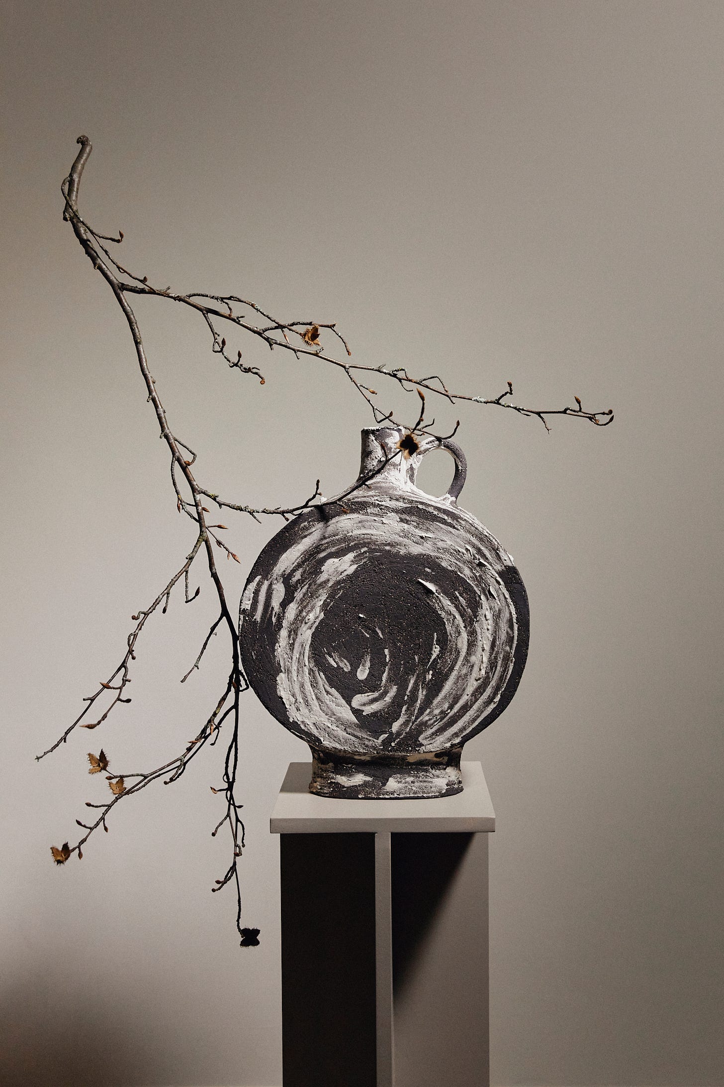 A large round vessel on a plinth with a bare branch balanced on it upside down.