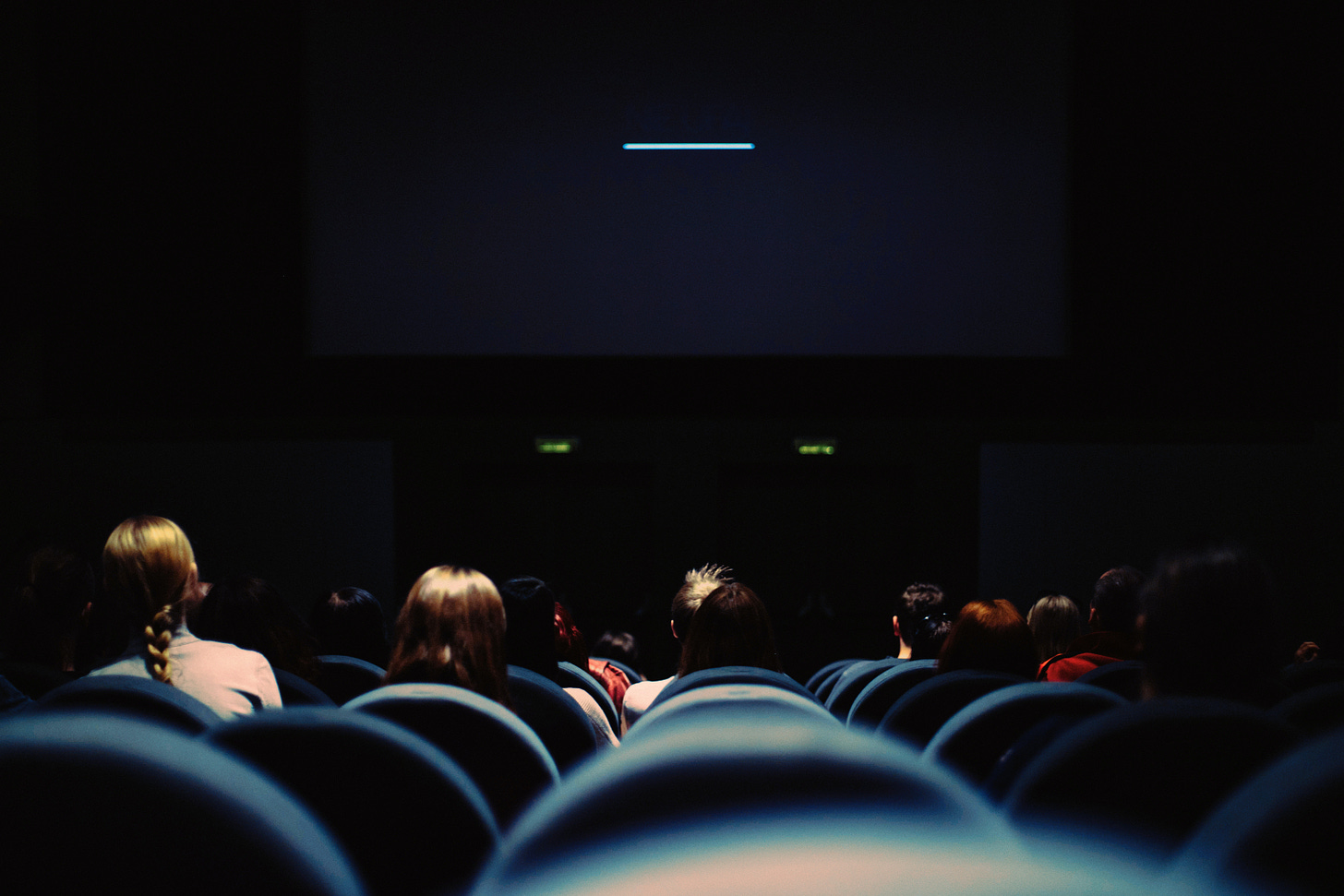 Behind a crowd of people. seated in a dark movie theater.