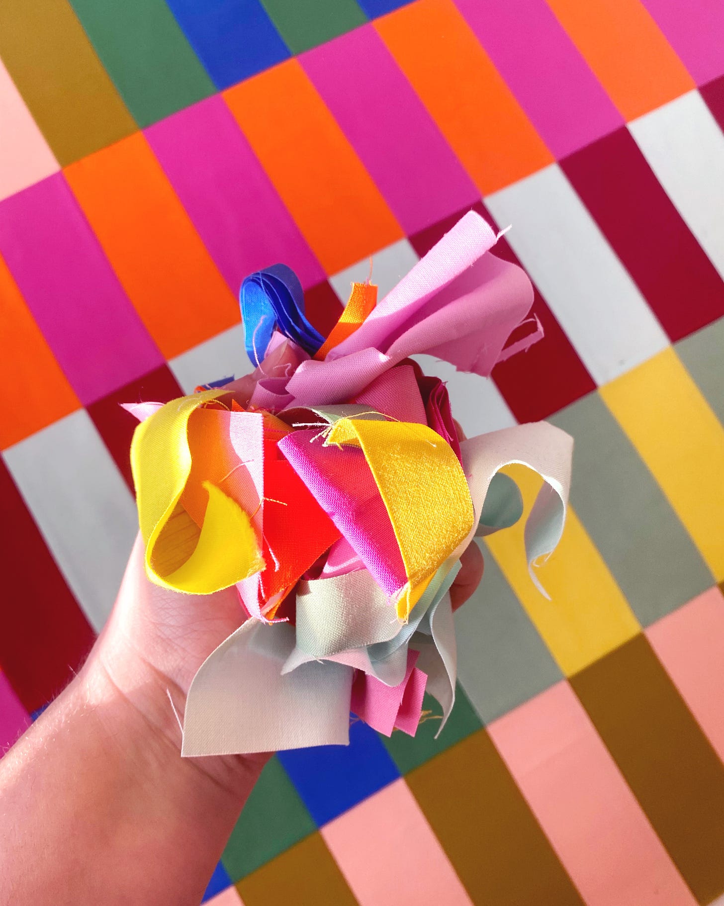 Hand of a white person holds colorful scrap fabrics in front of a colorful quilted background