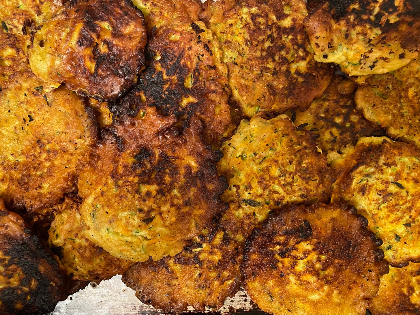 A tray of large, golden brown zucchini fritters piled on top of each other.