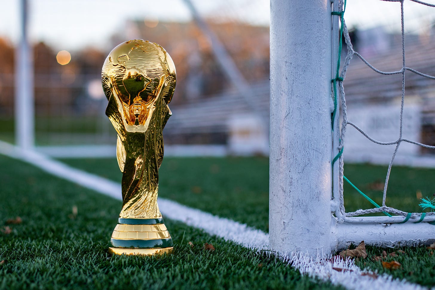 A World Cup trophy sits on a soccer pitch in front of the goal line.