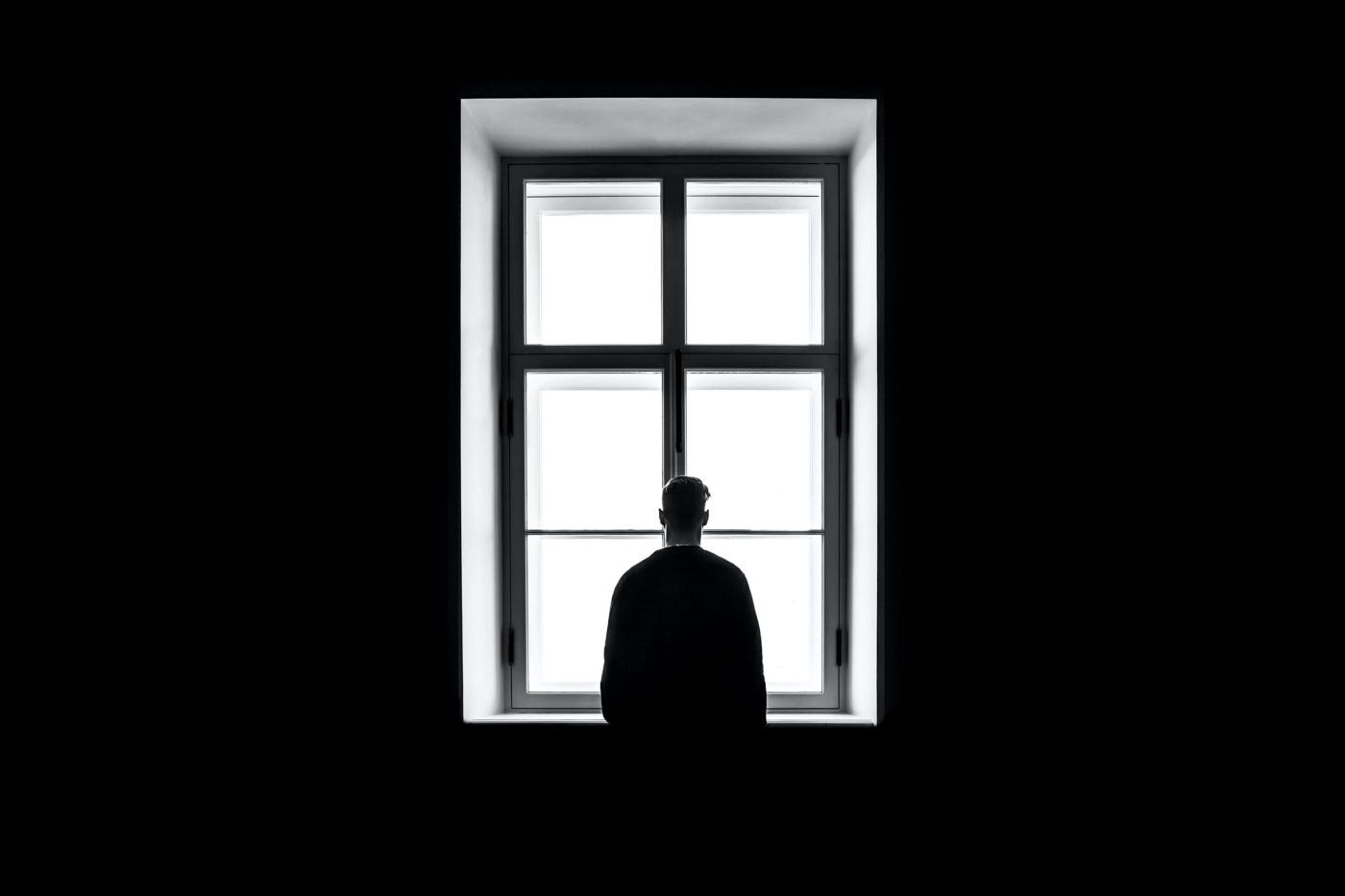 A silhouette of a man looks out of a large window with nothing discernible on the other side