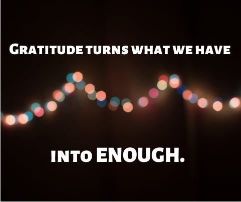 "Gratitude turns what we have into enough," is written across a dark background with a garland of blurred lights in the background.