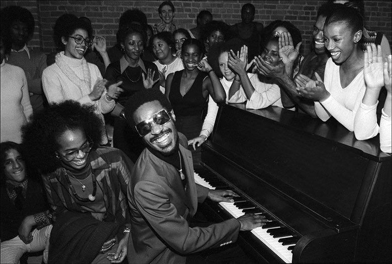 Stevie Wonder sitting at a piano entertaining students at the Dance Theater of Harlem in New York