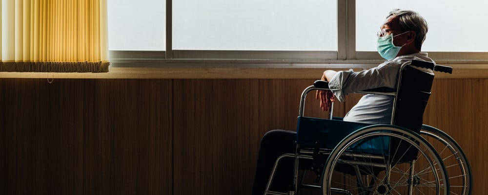 Panoramic asian elderly man wear mask sitting in wheelchair while looking out the window in nursing home or hospital.