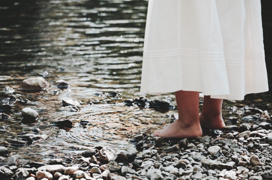 A girl in a long white dress stands in a riverbed.