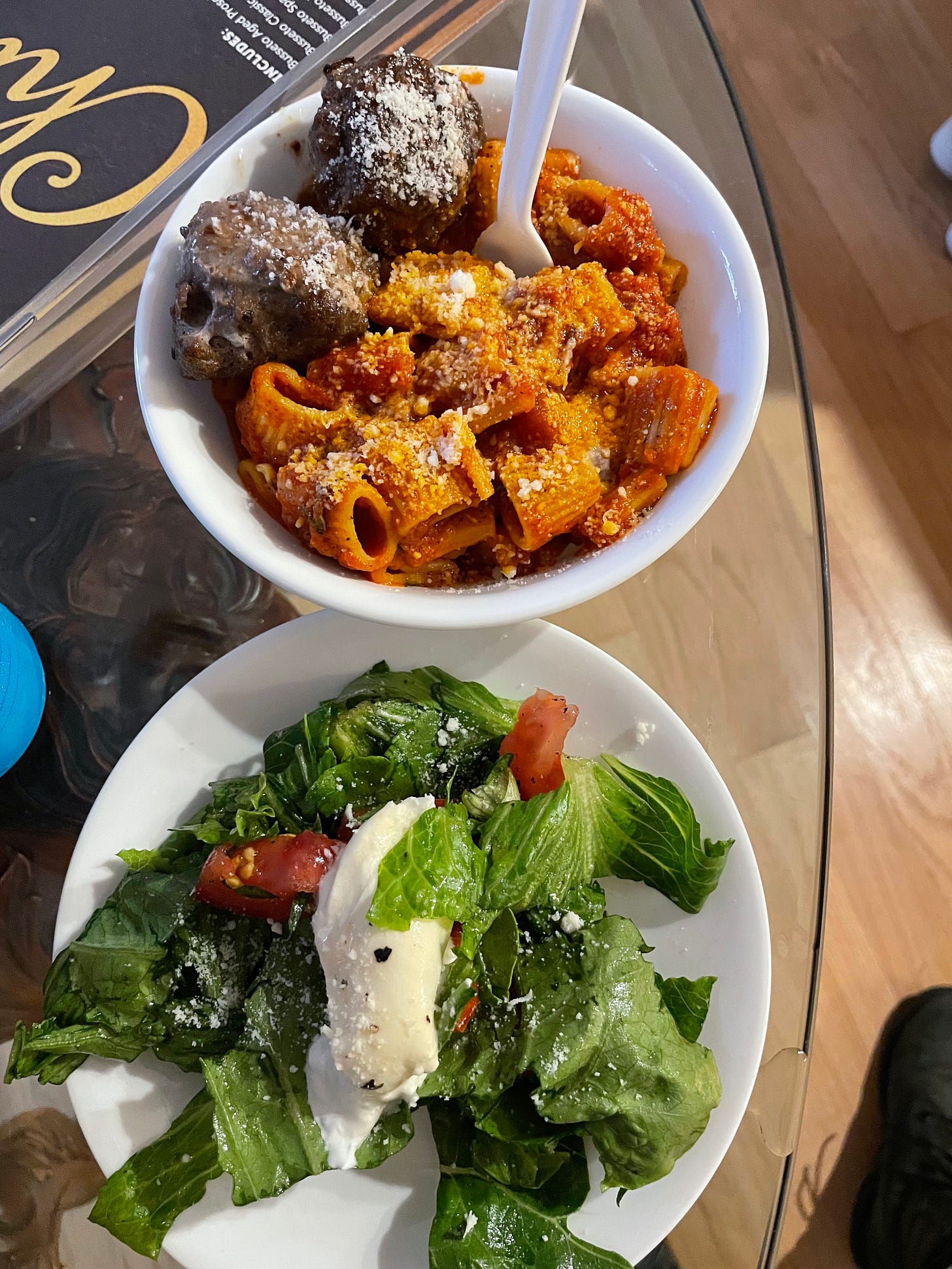 bowl of pasta and meatballs next to green salad with tomato and burrata