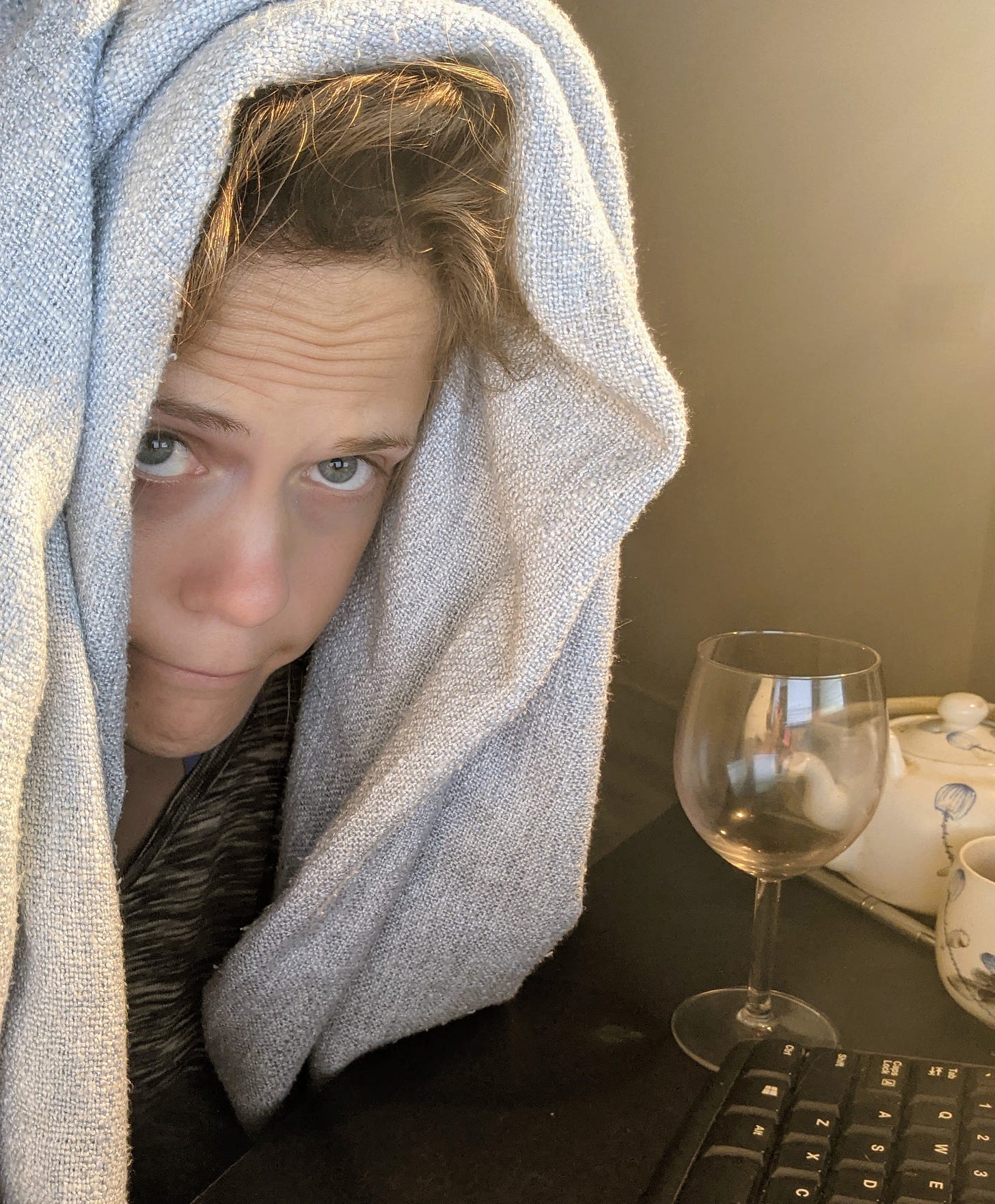 a white woman with a blanket over her head making a goofy face and holding a glass of red wine