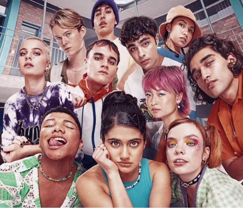A photo of a large group of teenagers of various genders, pulling a variety of faces, and wearing very nineties-style clothes, jewelry, make-up and hairstyles.