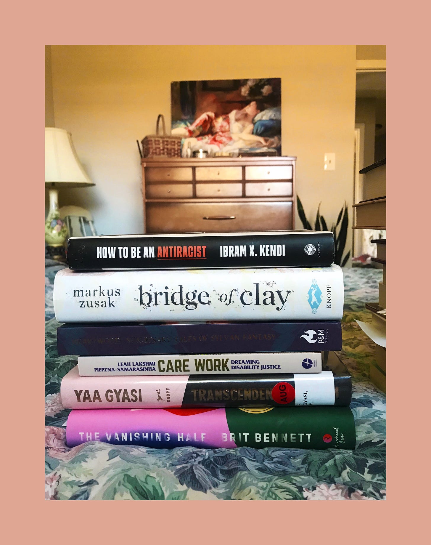 the six books mentioned below, stacked on a blue floral comforter on a bed. a dresser is in the background.