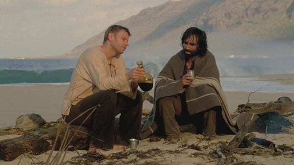 Jacob (Mark Pellegrino) and Ricardo (Nestor Carbonell) sit on a beach. Ricardo is wet and covered with a blanket. Jacob holds a bottle of wine.