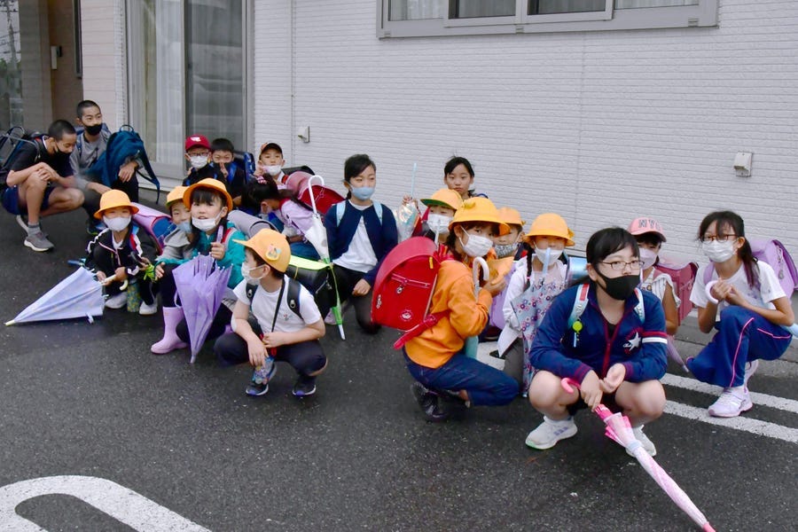 Elementary school students find shelter near a building on their way to school soon after a report of North Korea's missile launch, in Misawa, Aomori prefecture, northern Japan Tuesday, Oct. 4, 2022.
