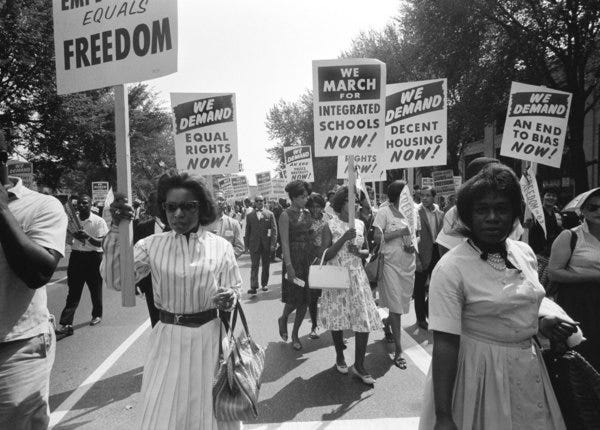 A marching group of black protesters from the civil rights era carry signs demanding equal rights under the law.