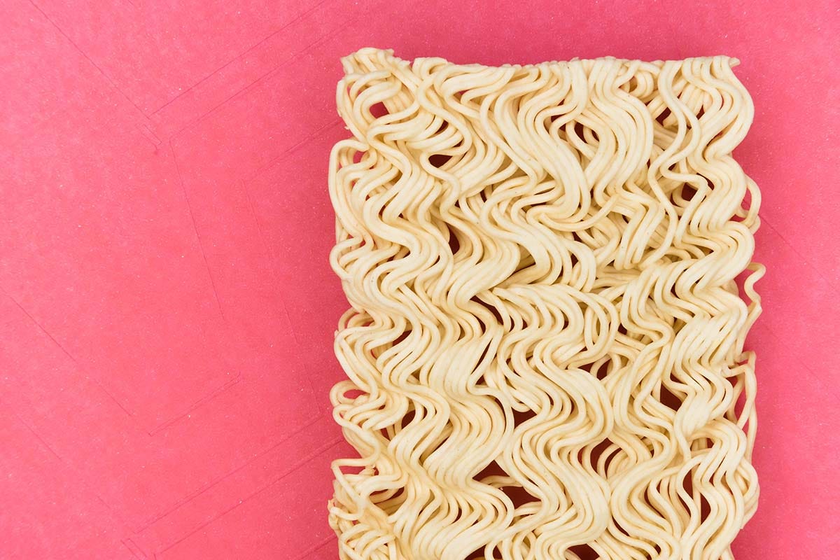 A block of ramen noodles on a fuschia background.