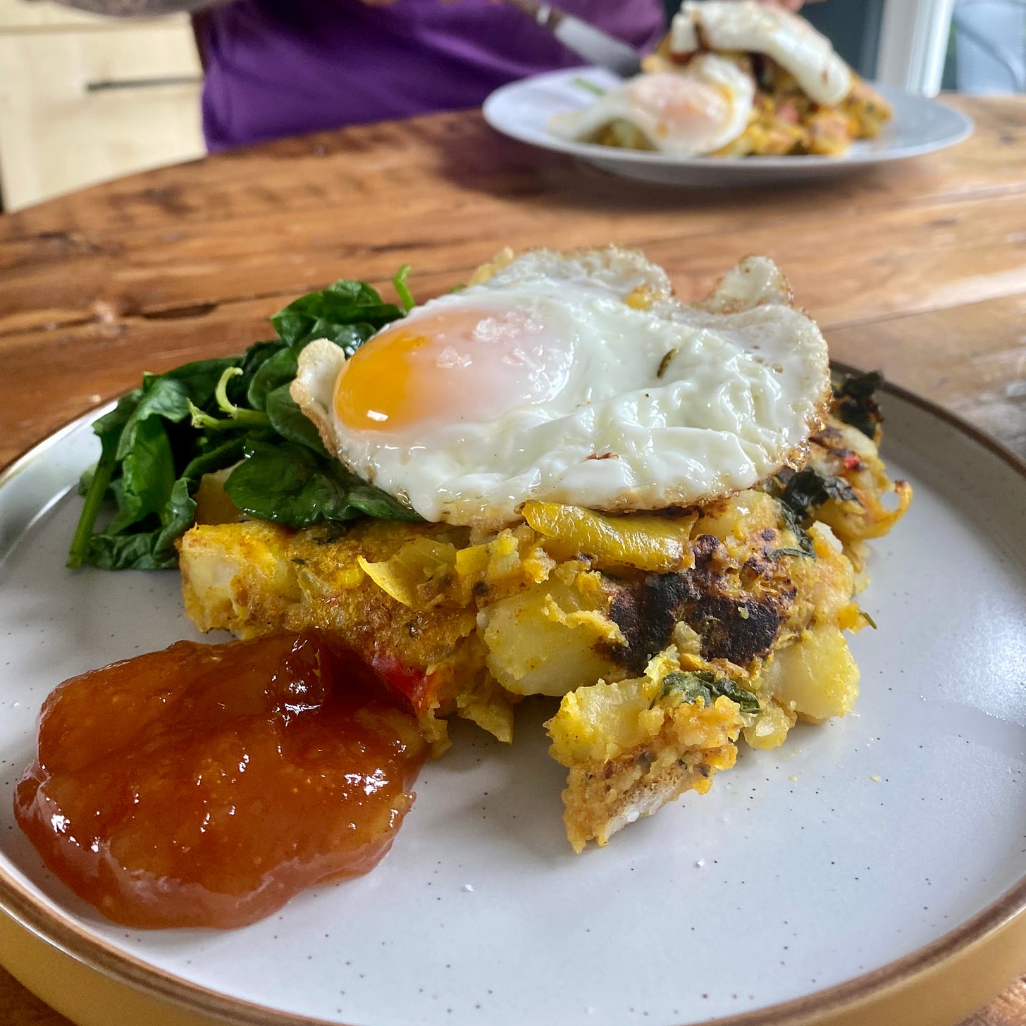 Plate with mango chutney, fried egg, wilted spinach and bubble and squeak made from Bombay potatoes