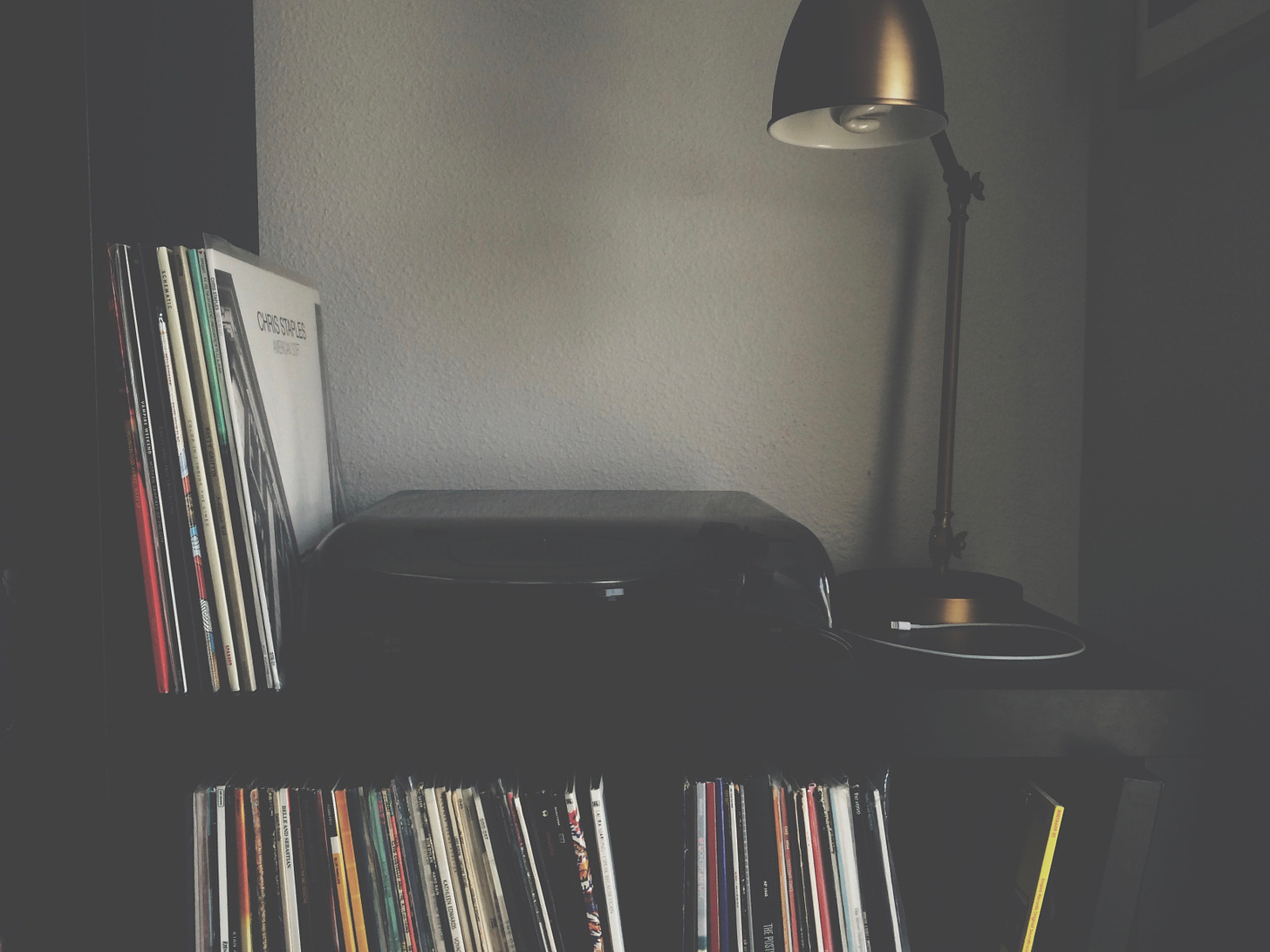 a record player with vertical stacks of records next to and on shelves underneath. An arm-style lap next to it.