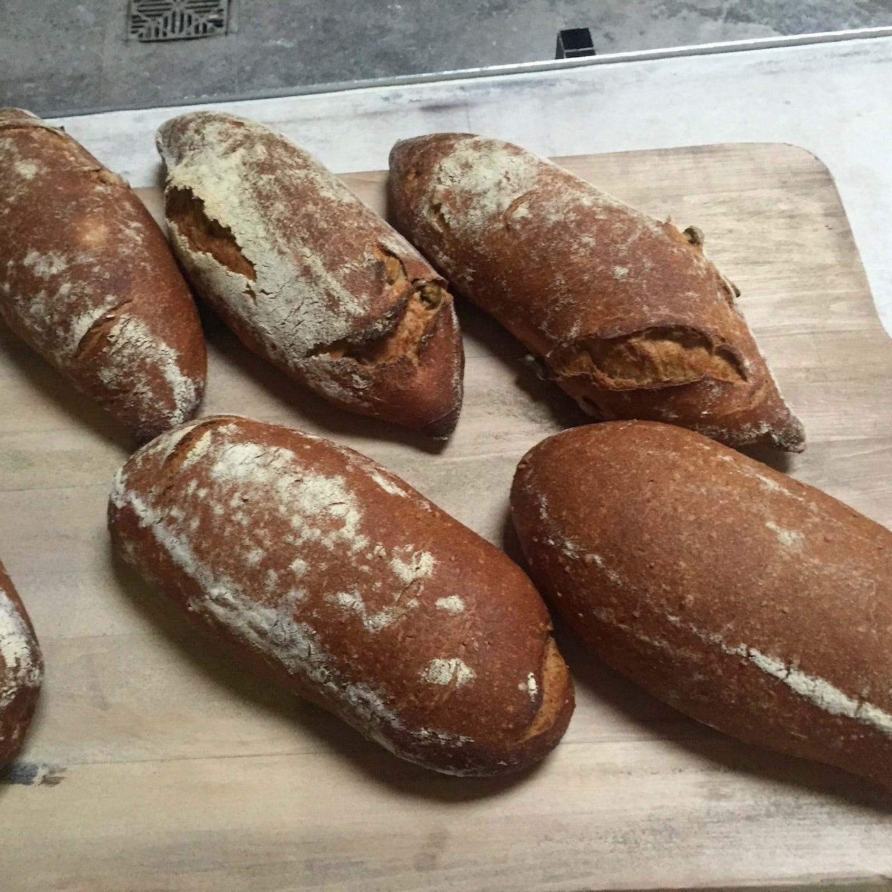 Five unscored golden brown loaves on a bread baking peel.