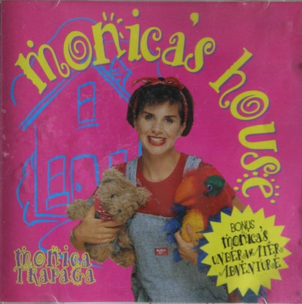 Monica Trapaga on a CD cover in red shirt and blue overalls holding a teddy and a soft toy parrot
