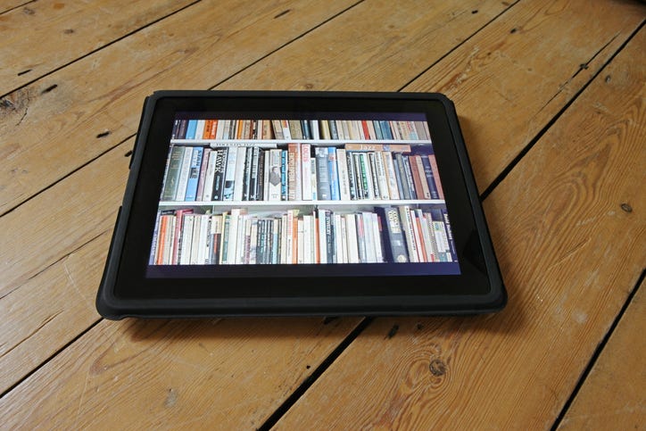 ipad com imagem colorida de várias lombadas de livros em uma estante branca.