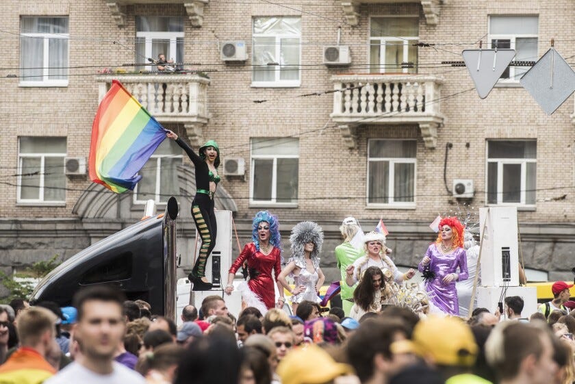 Men in drag ride on a float amid a crowd on a street