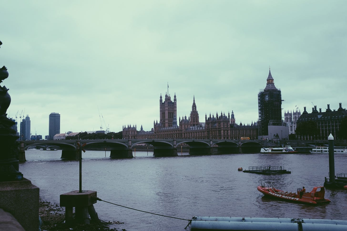 London's Houses of Parliament sit on the far side of the Thames. The day is dark and grey and the 35mm photograph is grainy and underexposed, the scene captured at a slightly haphazard angle