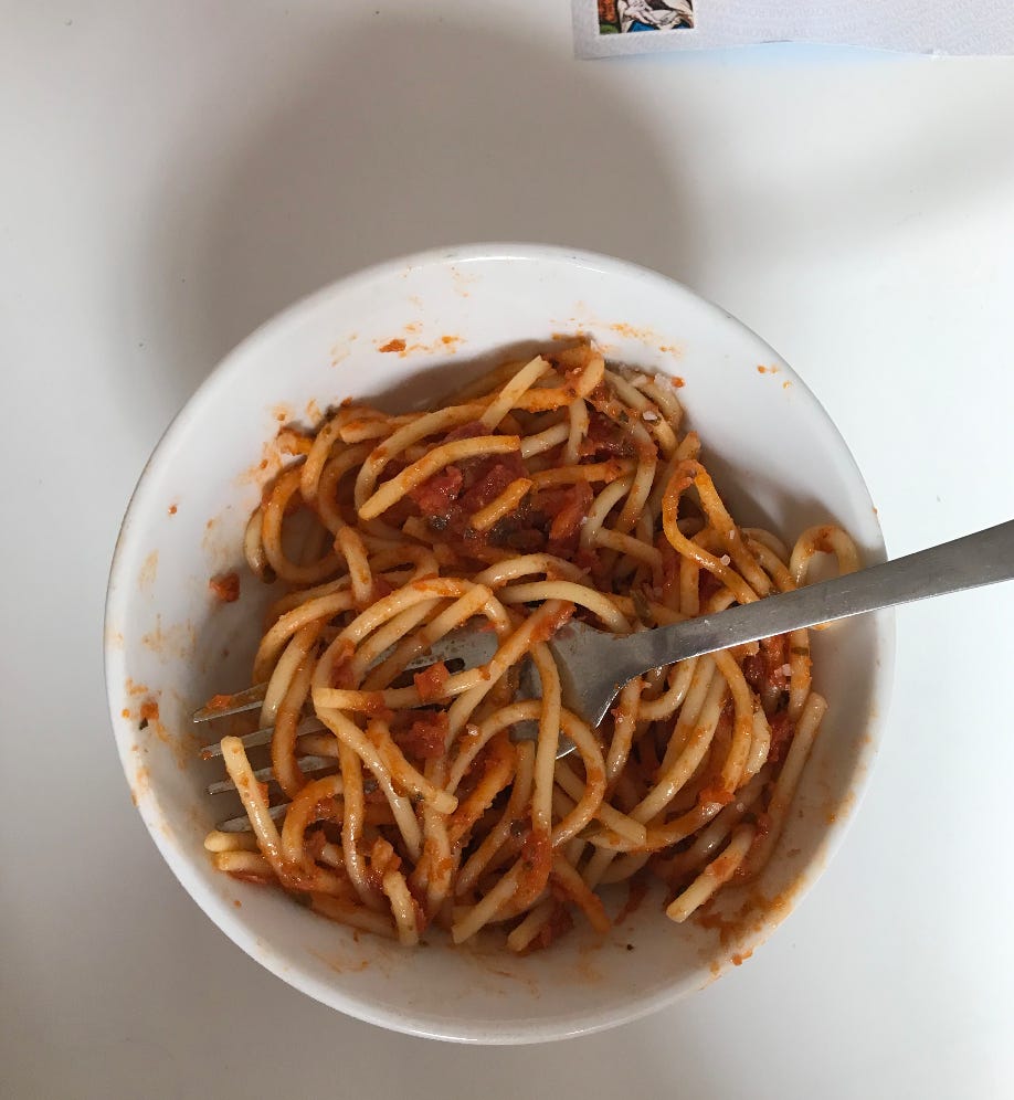 A photo of a bowl of orangey spaghetti from above. The background and bowl are both white. A metal fork prods in from the right, entangles the lengths. To the top edge of the photo, mostly out of shot, a sliver of a stamped envelope. 