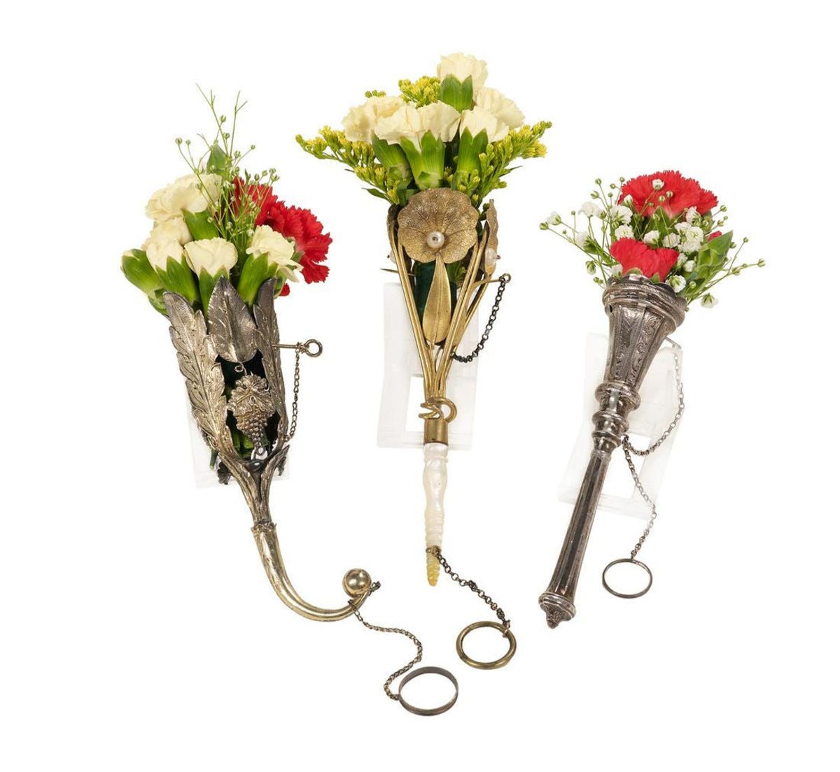 Three Victorian tussie-mussies, late 19th century: a silver thistle-form cup with embossed foliate panels and leaf-wrapped handle, chained pin and finger ring, 6” l; a gilt metal openwork conical cup with floral trelliswork and rococo scrolls, nacre handle and bodice pin, 5” l; and a gilt metal openwork conical cup embossed with acorns and foliate scrolls, acanthus scroll handle and bodice clip