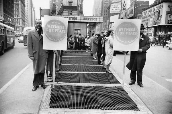 People at a demonstration outside the armed forces military recruitment center in Times Square in 1961. Two men carry signs that read, “Quaker witness for peace.” 