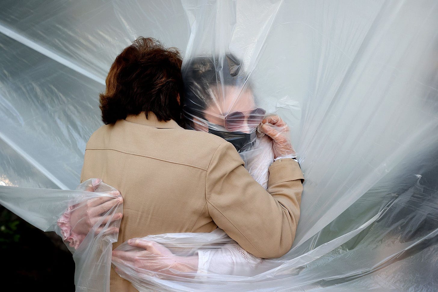 Olivia Grant, right, hugs her grandmother, Mary Grace Sileo, through a plastic drop cloth hung up on a homemade clothes line in Wantagh, N.Y.