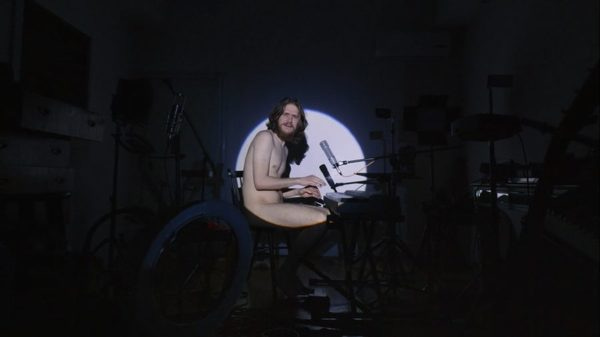 Bo Burnham sentado nu em frente ao seu teclado, iluminado apenas por um holofote