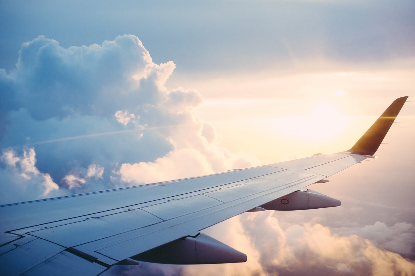 view from inside a plane of the wing, clouds, and the sun setting