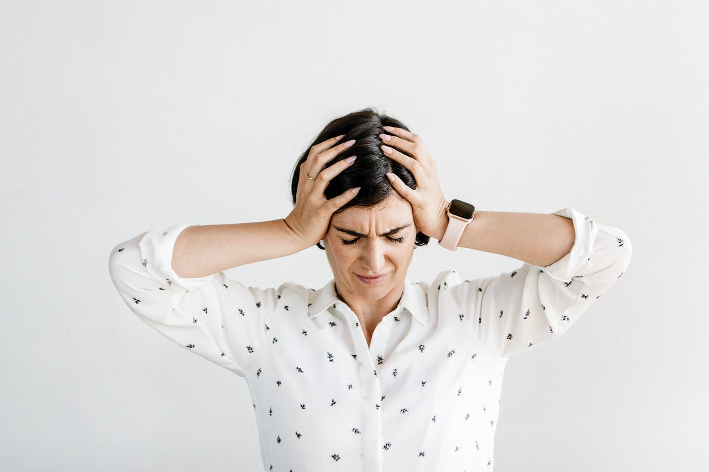 A stressed woman with dark hair holds her head in between her hands in a sign of frustration.