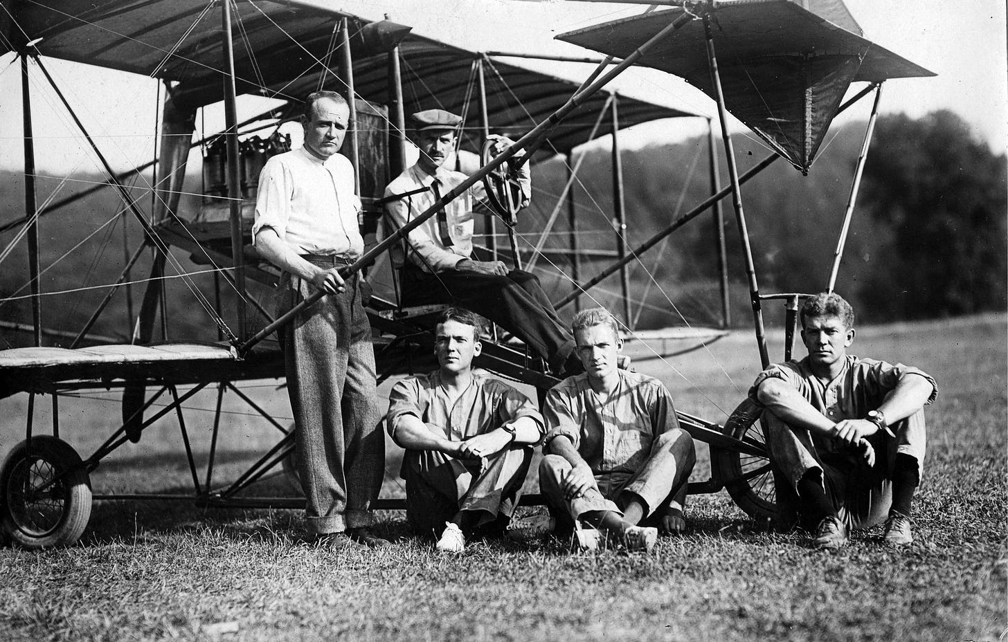Glenn Curtis sits at the controls of a Curtis A-1 plane. Seated in front of the plane are John Rodgers, John Towers, and Theodore Ellyson. An unidentified man leans against the plane next to Curtis,. (US Navy photo)