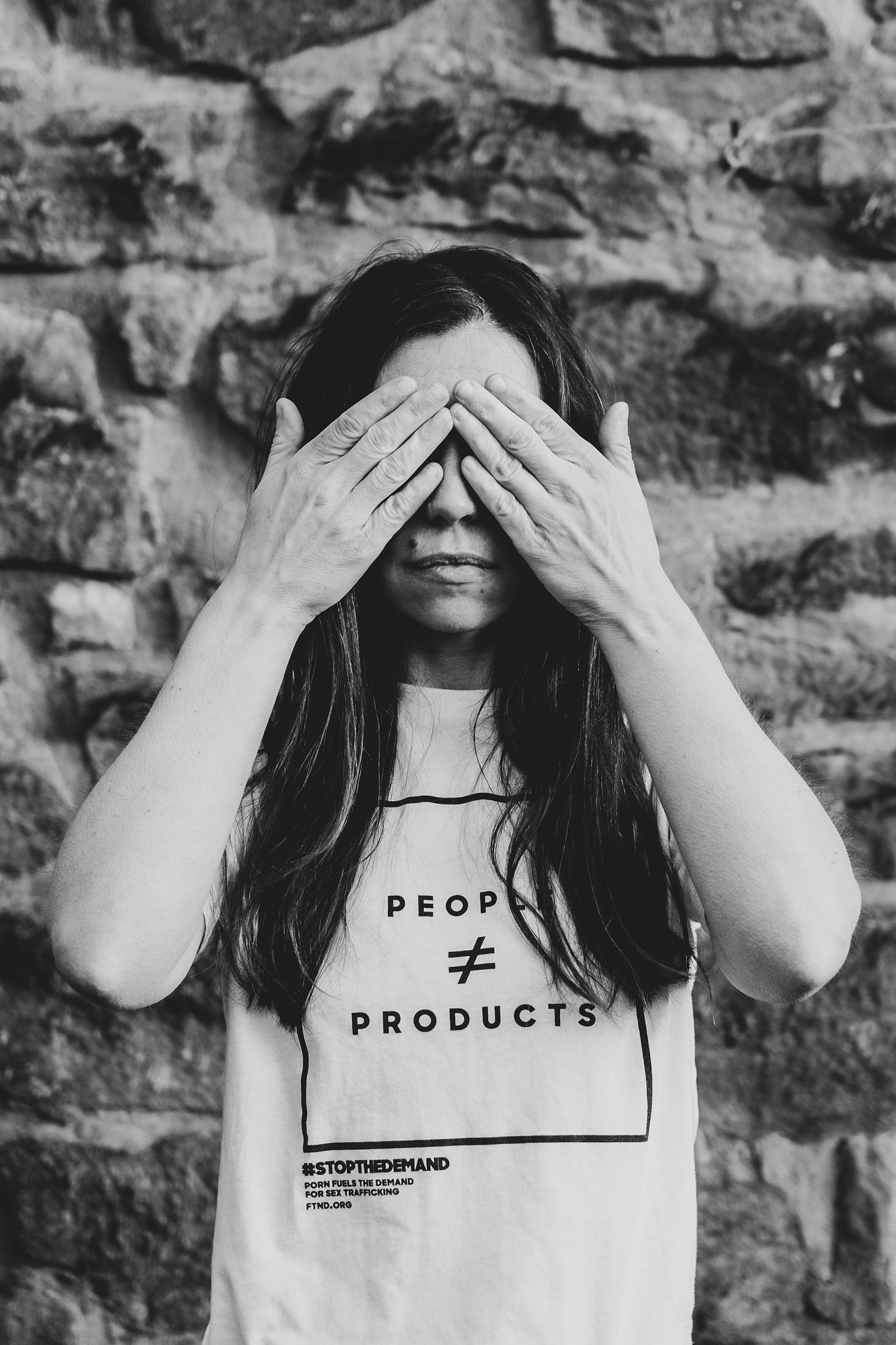 Black and White photo of woman covering her eyes with her hands wearing a stop the demand t-shirt from the company fight the new drug