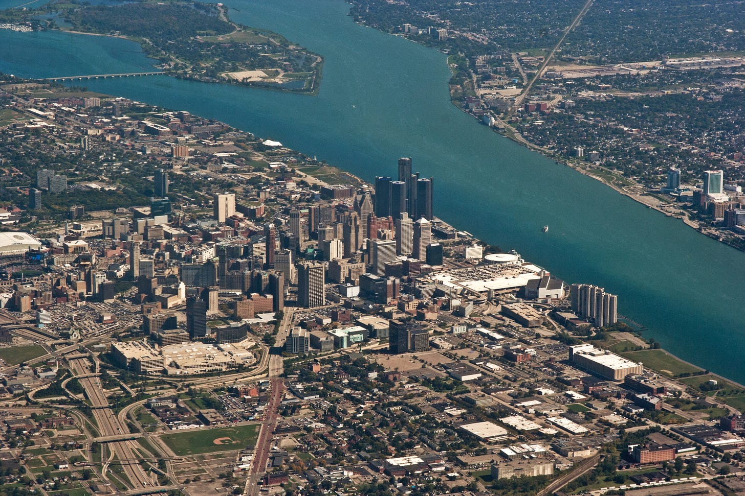 An aerial shot of Detroit, looking northeast to Ontario Canada with Belle Isle visible in the center of the Detroit River